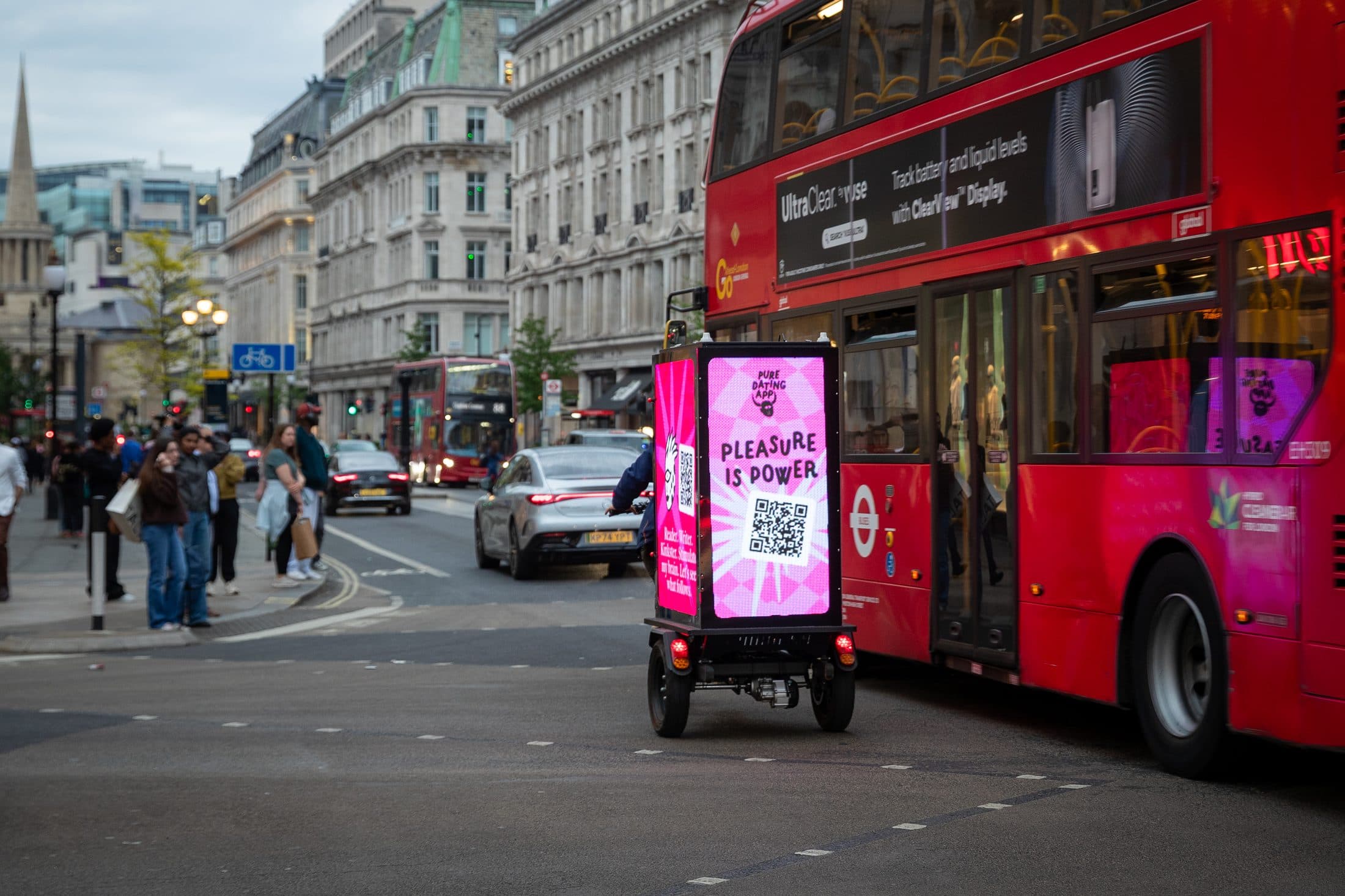Digital AdBike screens glowing at dusk beside a London red bus