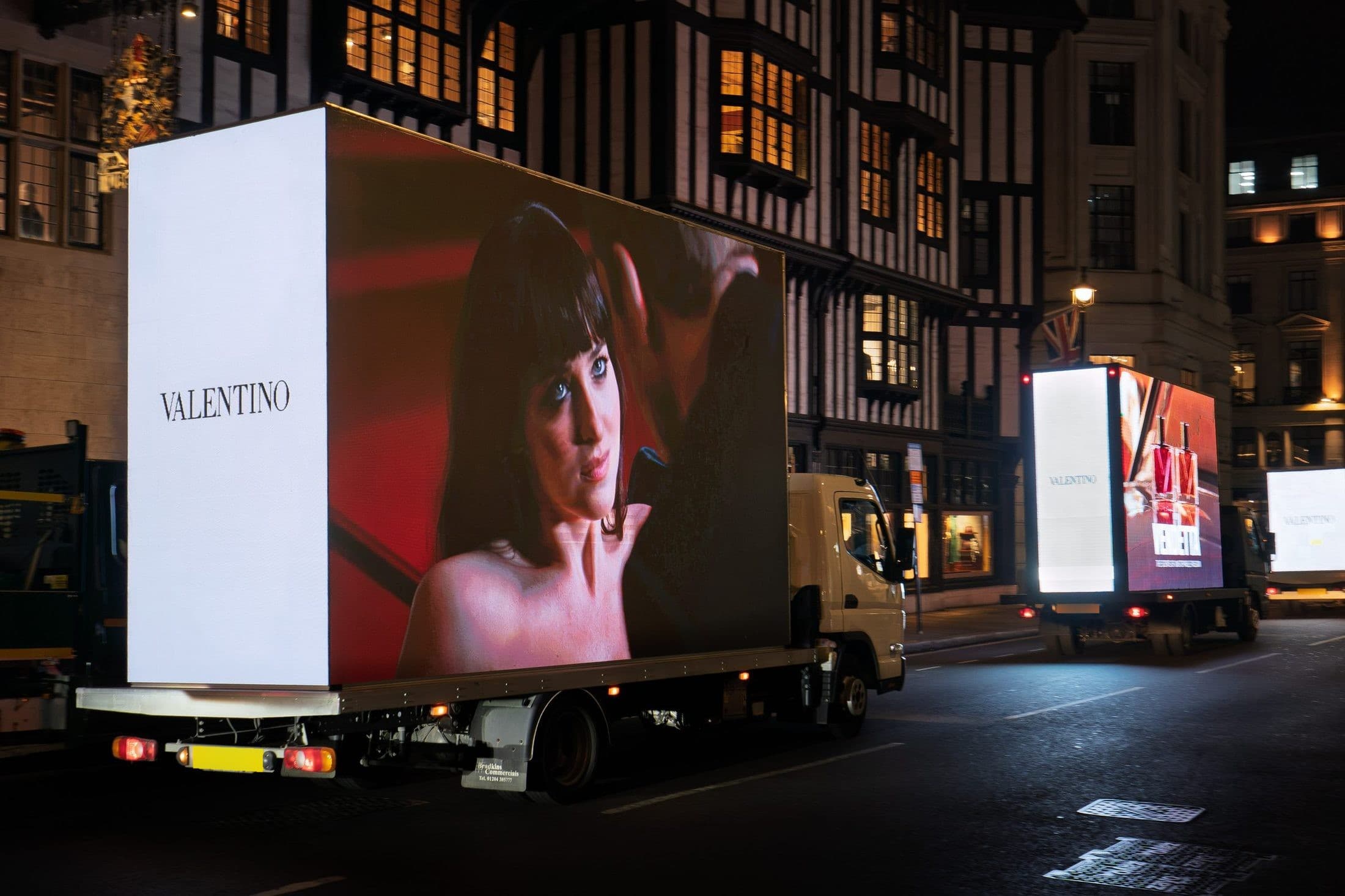 Three Monster Digital AdVans in convoy leaving Liberty at night with the Valentino Vendetta campaign on their LED screens, Soho, London