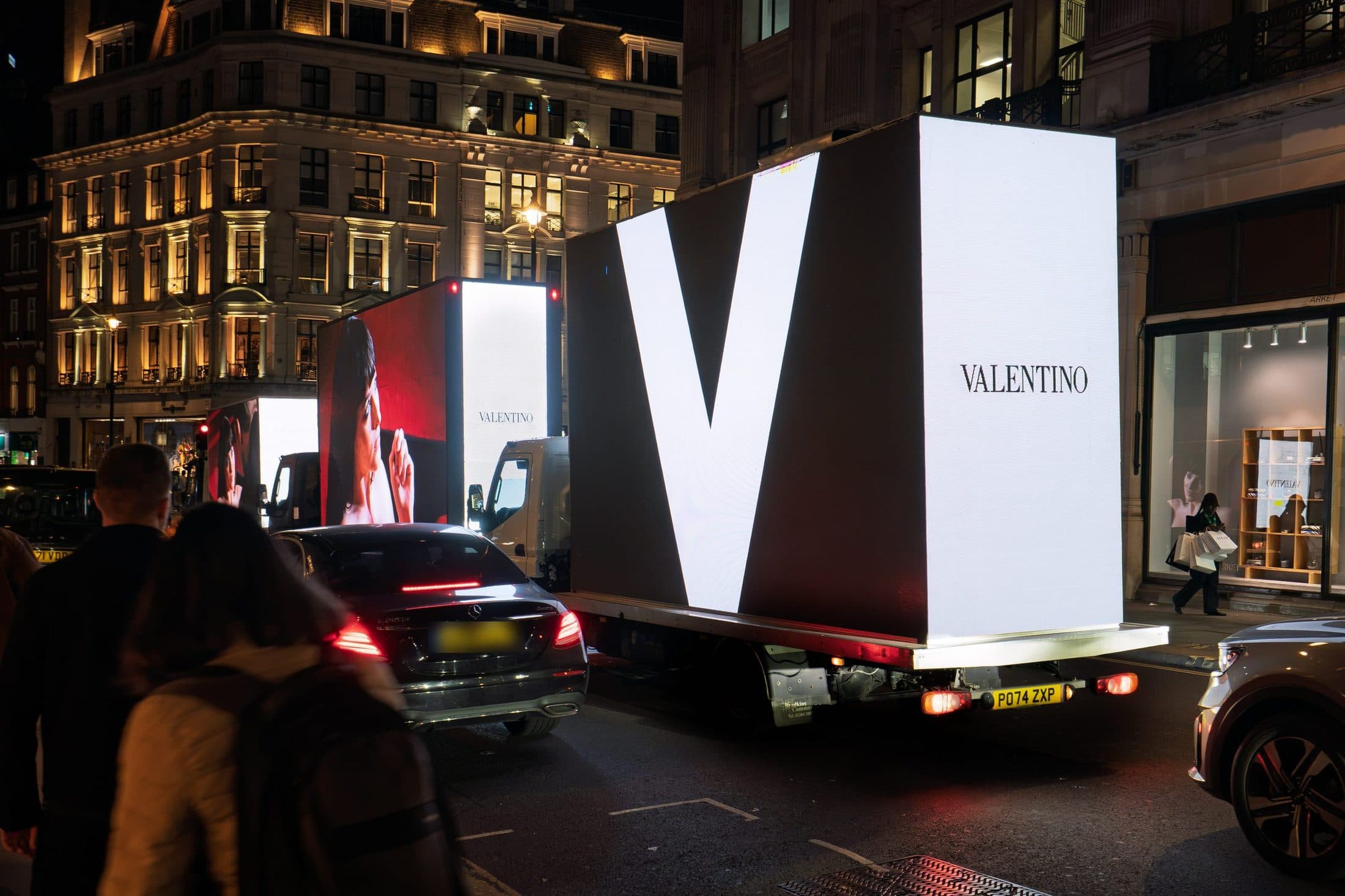 The giant white V and the VALENTINO wordmark on the back of a Monster Digital AdVan on Regent Street at night, with the convoy ahead