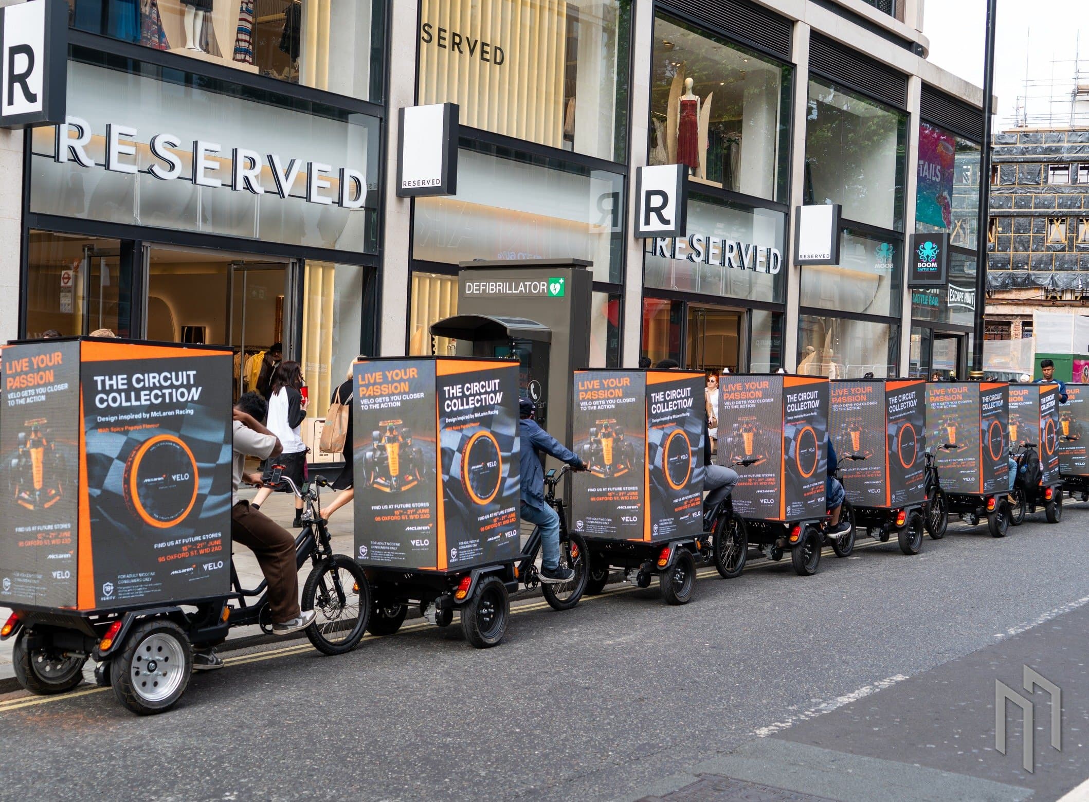 The ten-bike Velo x McLaren F1 AdBike fleet riding past the Reserved store on Oxford Street