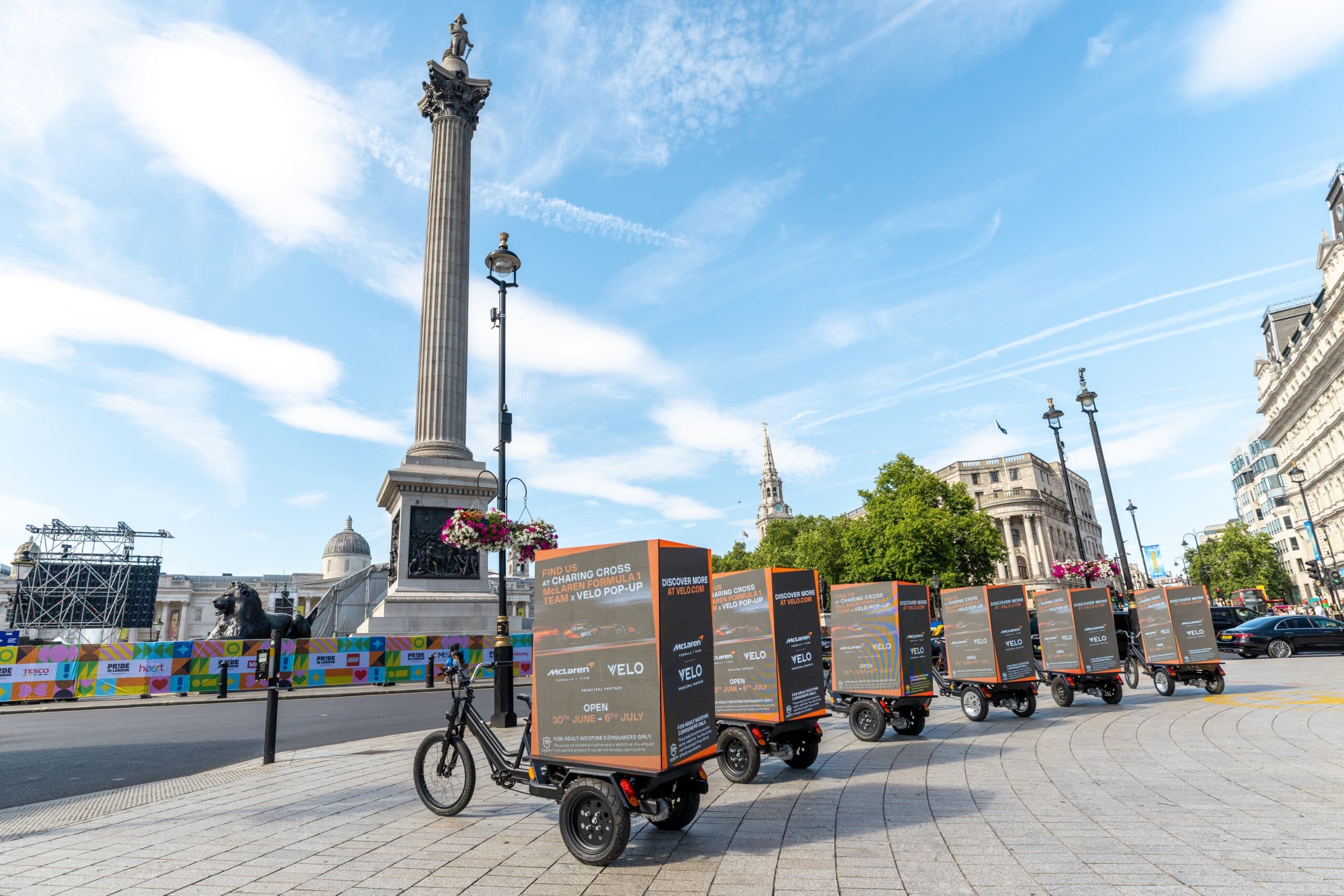 Velo x McLaren F1 Digital Billboard Bikes passing Trafalgar Square