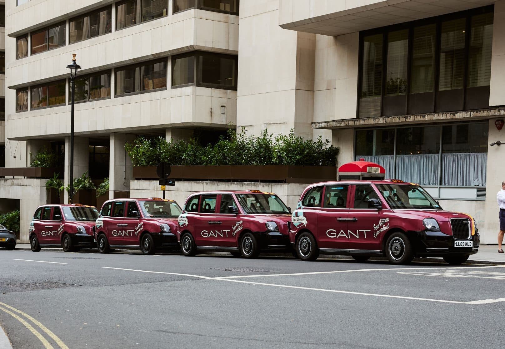 Four GANT wrapped electric London taxis parked in a row on a city street