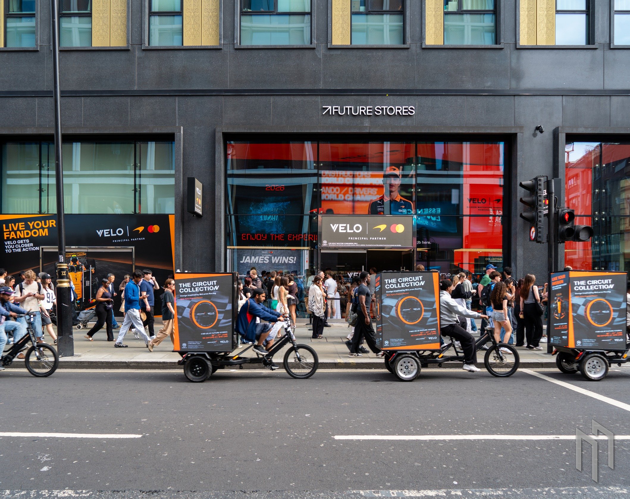 Velo x McLaren Digital AdBikes riding past the Future Stores pop-up on Oxford Street